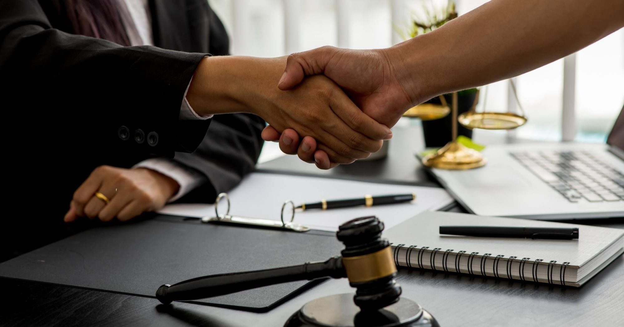 Lawyer and client shaking hands with legal documents and a gavel on the desk – Eleven Legal consultation services