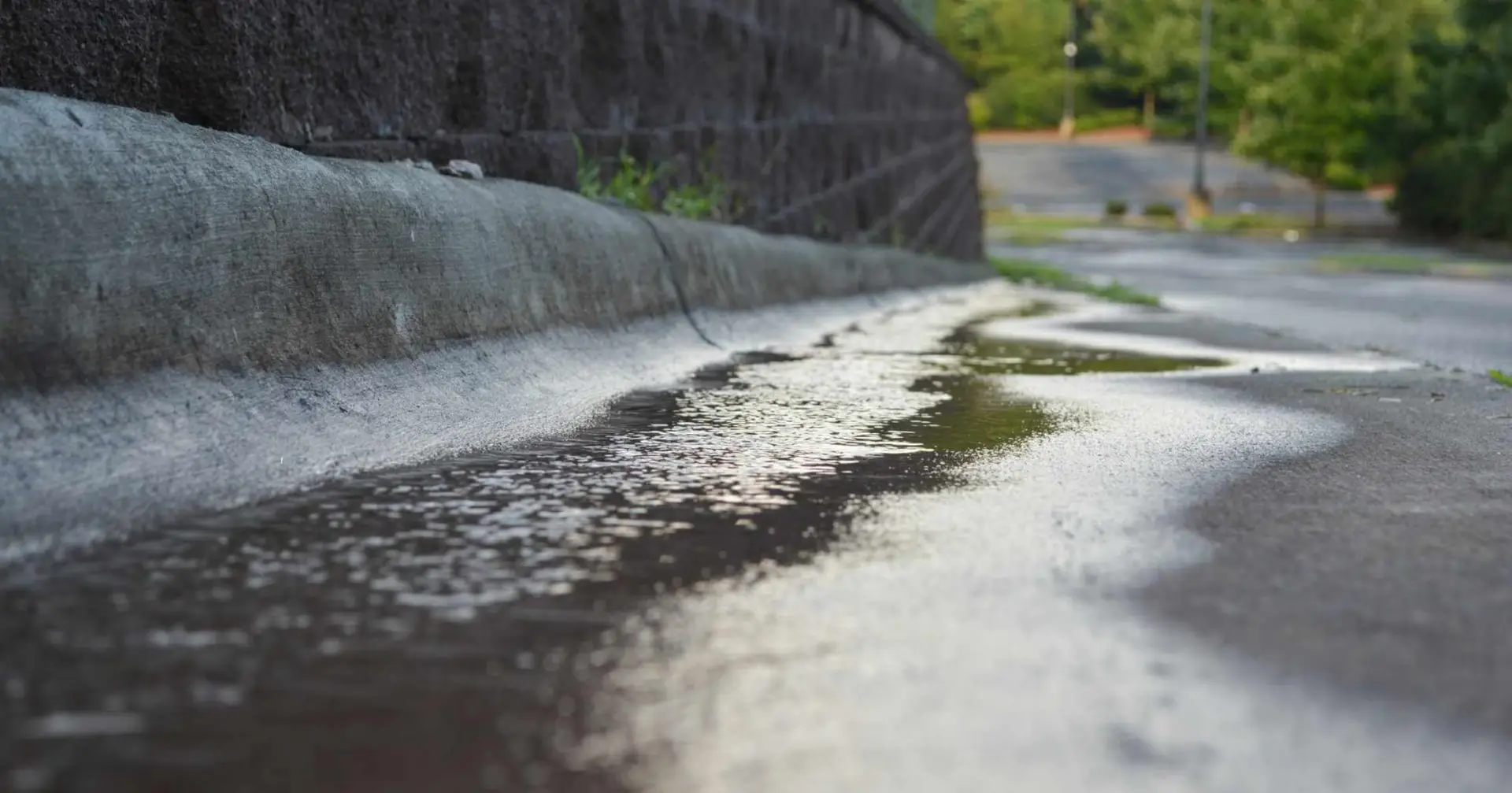 Stormwater runoff flowing along a concrete path after rainfall.