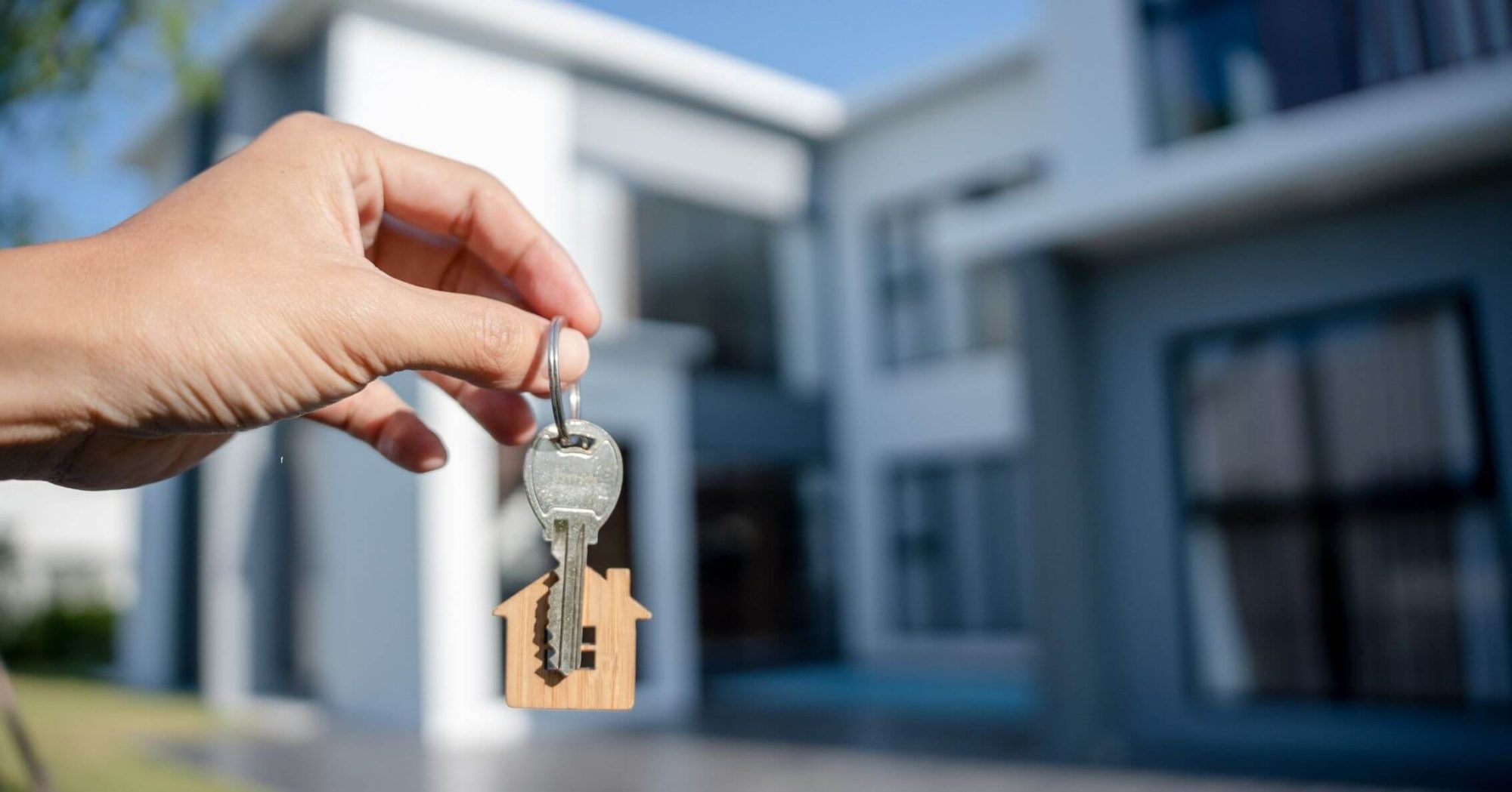 Hand holding house keys in front of a modern home – Eleven Legal property settlement services