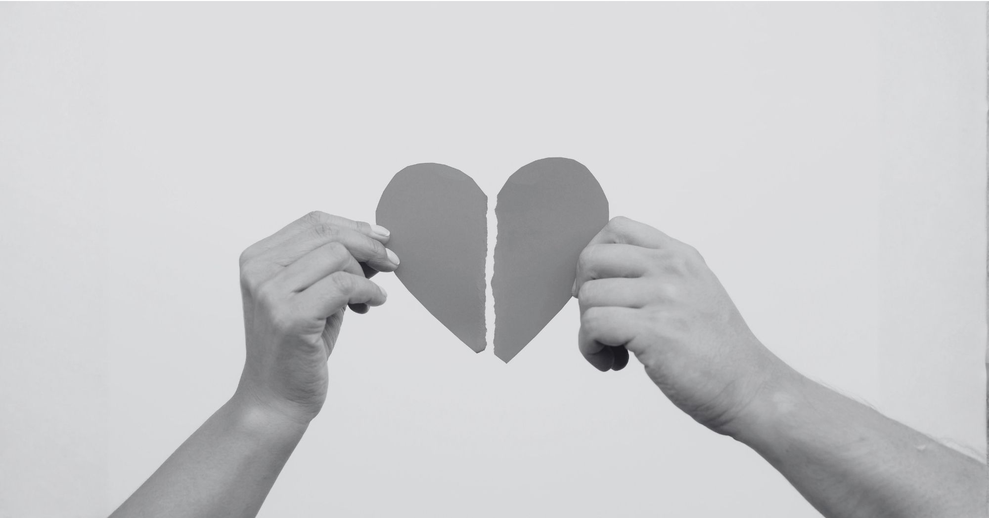 Paper heart being pulled apart by two hands